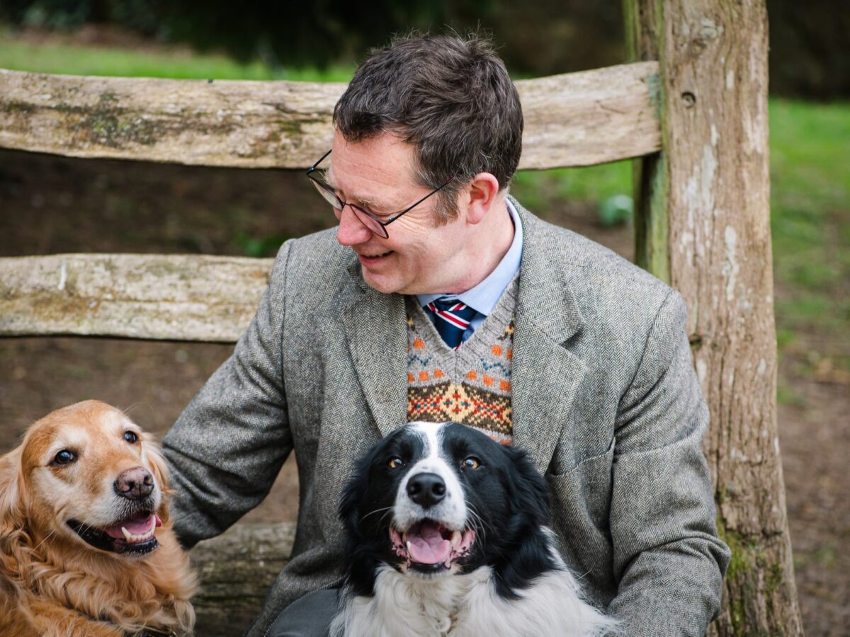 Dr James Hunt sitting outdoors with a golden retriever and a border collie